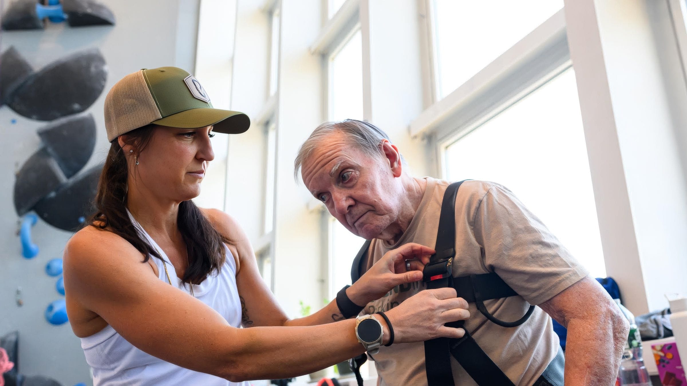 Molly Cupka at the climbing gym Molly Cupka fitting a climbing harness on an older participant at the gym